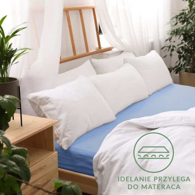 Prześcieradło jersey z gumką 60x120 w kolorze niebieskim, leżące na łóżku. Jest dopasowane do materaca, z widoczną gładką fakturą.
