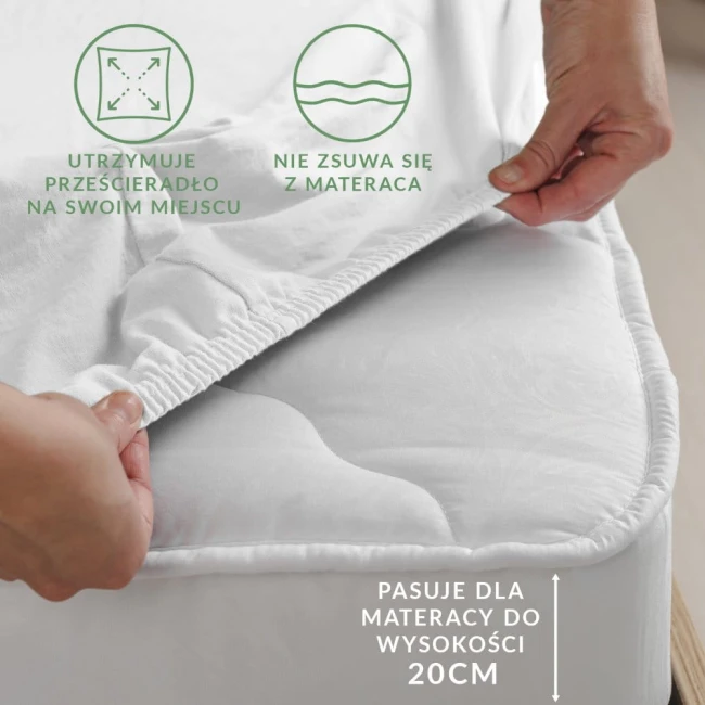 Prześcieradło jersey z gumką w kolorze białym, rozmiar 200x220 cm, naciągnięte na materac. Widoczne elastyczne brzegi zapobiegające zsuwaniu się. Ujęcie z boku, ręka trzymająca krawędź, co pokazuje wygodę zakupu. Proste tło.