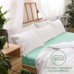 Prześcieradło jersey z gumką 160x200 w kolorze morskim, rozłożone na łóżku z jasną pościelą. Widoczne białe poduszki w tle oraz drewniana rama łóżka. Tło jasne, z rośliną w doniczce, co podkreśla aranżację sypialni.