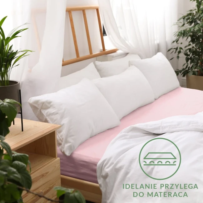 Prześcieradło jersey z gumką 90x200 w kolorze róż kwarcowy, rozłożone na łóżku z białymi poduszkami. Widoczne gładkie wykończenie, dobrze dopasowane do materaca. Tło z naturalnym oświetleniem i roślinnymi dekoracjami w aranżacji sypialnianej.