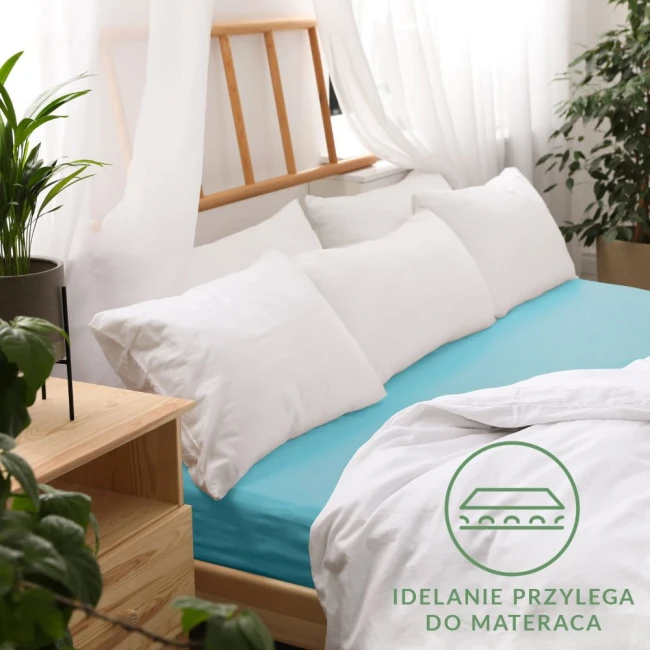 Prześcieradło jersey z gumką 200x220 w kolorze turkusowym, rozłożone na materacu, z białymi poduszkami w tle. Tło jasne, z roślinnością i drewnianym meblem. Widoczne logo w dolnej części zdjęcia, podkreślające doskonałe przyleganie do materaca.