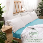 Prześcieradło jersey z gumką w kolorze turkusowym, rozmiar 160x200, nałożone na łóżko z białymi poduszkami. Ujęcie z boku, pokazujące sposób przylegania do materaca.
