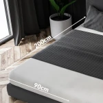 Prześcieradło frotte z gumką w kolorze jasnego beżu o wymiarach 90x200 cm, rozłożone na materacu. Na zdjęciu widoczny jest zbliżenie na fakturę materiału oraz oznaczenia wymiarów. W tle naturalne wnętrze z roślinnością i oknem.