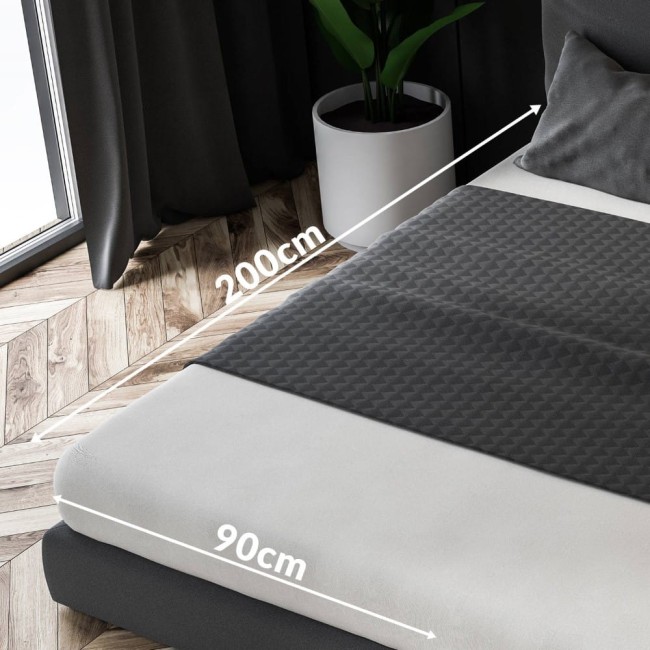 Prześcieradło frotte z gumką w kolorze jasnego fioletu o wymiarach 90x200 cm, leżące na materacu. Widoczne są oznaczenia wymiarów, a w tle roślina w doniczce oraz zasłony. Tekstura materiału jest miękka i elastyczna.