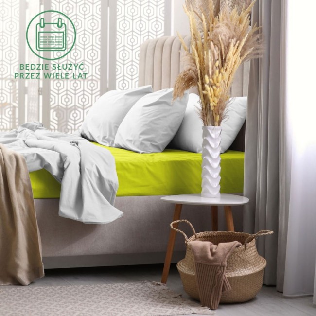 Prześcieradło frotte z gumką 120x200 w kolorze limonka, leżące na łóżku z białymi poduszkami. Produkt z widoczną teksturą materiału, w otoczeniu naturalnych dekoracji, takich jak wazon z suszonymi kwiatami i kosz na podłodze.