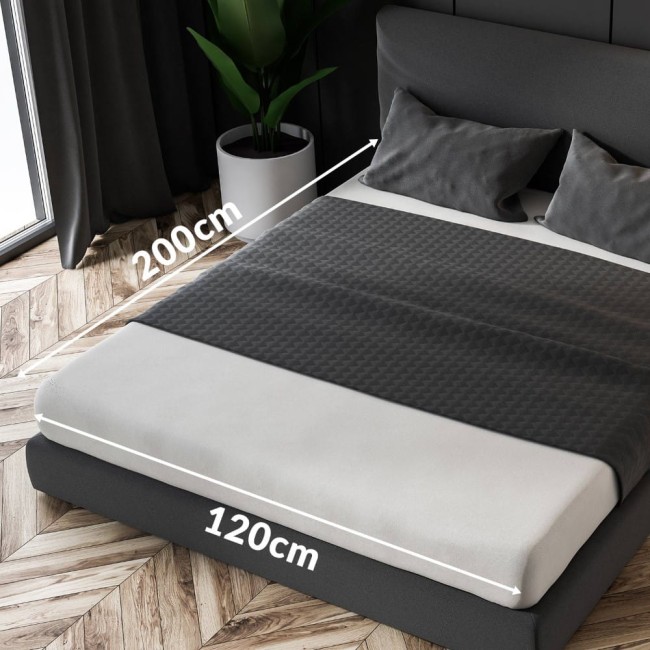 Prześcieradło frotte z gumką 120x200 cm w kolorze niebieskim, leżące na łóżku. Widoczne jest boki i górna część, z gumkowymi brzegami. W tle szara, tapicerowana głowa łóżka oraz poduszki. Drewniana podłoga i roślina w doniczce.