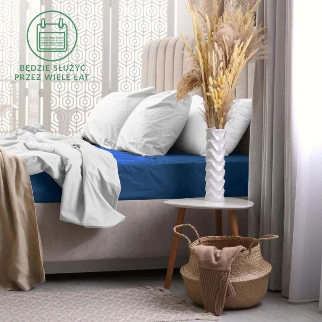 Prześcieradło frotte z gumką w kolorze chabrowym, rozłożone na materacu w sypialni, z widocznymi białymi poduszkami. Tło w stylu nowoczesnym z jasnymi zasłonami i dekoracjami.