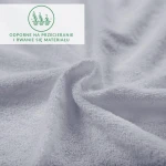 Prześcieradło frotte z gumką w kolorze popielatym, o gładkiej, teksturowanej powierzchni. Ukazane w zbliżeniu, w ruchu, z miękkim splotem włókien. Widoczna etykieta informująca o odporności na przecieranie i rwanie.