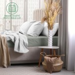 Prześcieradło frotte z gumką w kolorze szarym, rozłożone na łóżku z białymi poduszkami, z widoczną fakturą materiału. Mebel w tło w jasnym kolorze z beżowym kocem oraz dekoracyjnym koszem. Ujęcie z boku, na prostym tle w sypialni.