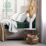 Prześcieradło frotte z gumką 140x200 w kolorze zieleni butelkowej, leżące na materacu. Otoczone białymi poduszkami i narzutą. W tle widoczna jasna zasłona i dekoracyjna waza z suszonymi kwiatami na stoliku. Proste tło w jasnych odcieniach.