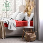 Prześcieradło frotte z gumką 160x200 w kolorze czerwonym, rozłożone na łóżku z jasną pościelą. Kąt ujęcia frontalny, podkreślający fakturę materiału. W tle białe zasłony, stół nocny z wazonem i suszonymi kwiatami. Widzoczny kosz z materiałem obok.