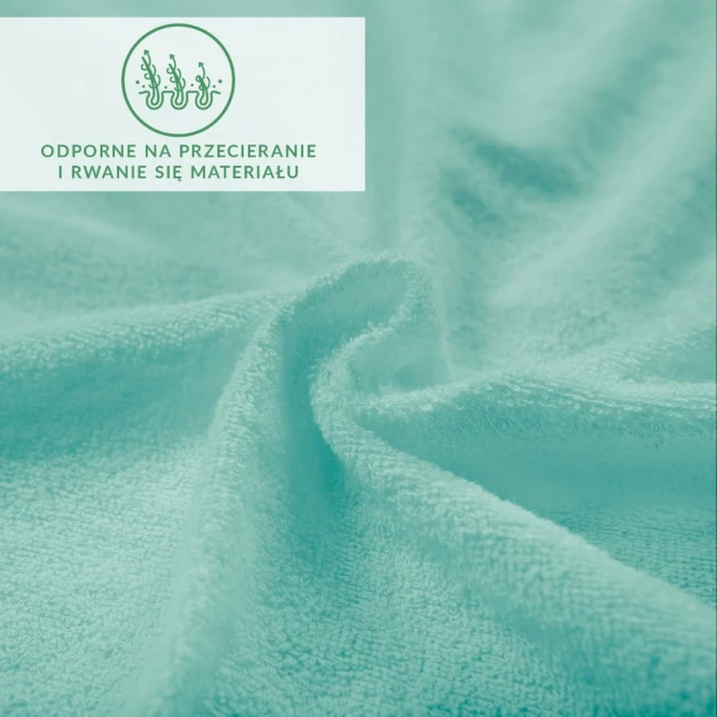Prześcieradło frotte z gumką w jasnym turkusie, z bliska, ukazuje miękką, teksturowaną powierzchnię materiału. Widoczne informacje o odporności na przecieranie i rwanie. Produkt leży rozłożony, co podkreśla jego elastyczność i funkcjonalność.