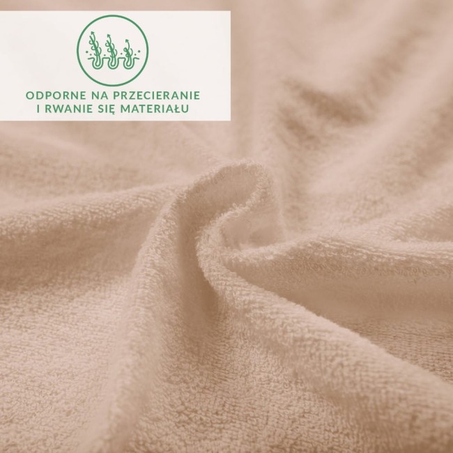 Prześcieradło frotte z gumką w kolorze beżowym, rozłożone na płaskiej powierzchni. Materiał teksturowany, przyjemny w dotyku. Widoczny napis informujący o odporności na przecieranie i rwanie materiału. Brak dodatkowych elementów dekoracyjnych.