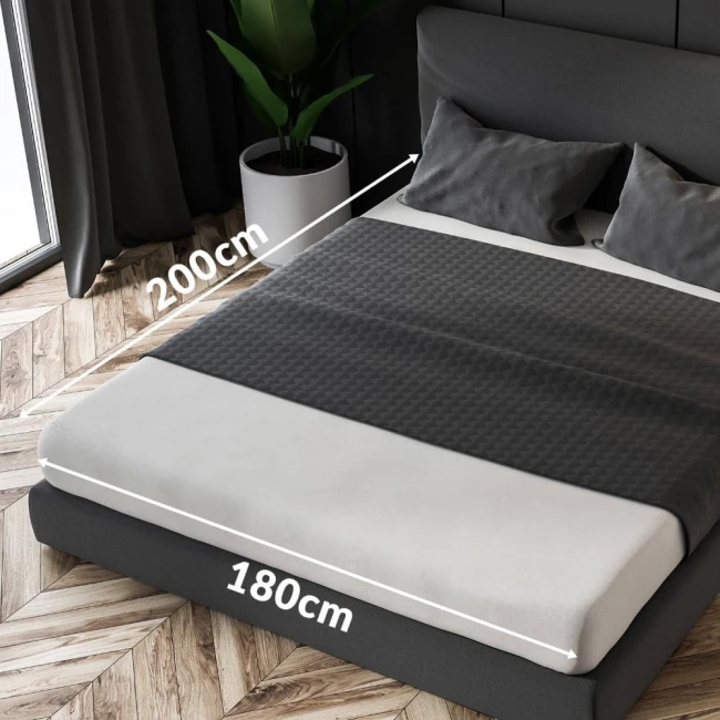 Czerwone prześcieradło frotte z gumką o wymiarach 180x200 cm, rozłożone na łóżku. Produkt ukazany z boku, z widocznymi wymiarami. Tło drewniane, z poduszkami w kolorze szarym na łóżku.