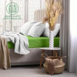 Prześcieradło frotte z gumką 180x200 w kolorze kaktus, rozłożone na łóżku. Widoczne miękkie tekstury niebieskiej narzuty oraz białych poduszek. W tle biały stół z dekoracyjnym wazonem i roślinami. Świetne do stylizacji nowoczesnej sypialni.