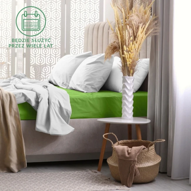 Prześcieradło frotte z gumką 180x200 w kolorze kaktus, rozłożone na łóżku. Widoczne miękkie tekstury niebieskiej narzuty oraz białych poduszek. W tle biały stół z dekoracyjnym wazonem i roślinami. Świetne do stylizacji nowoczesnej sypialni.