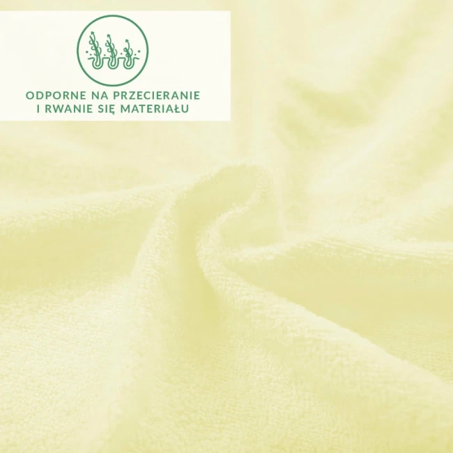 Prześcieradło frotte z gumką w kremowym kolorze, leżące na gładkiej powierzchni, ukazujące teksturę materiału. Widoczne logo oraz informacja o odporności na przecieranie i rwanie się materiału. Zbliżenie na delikatną fakturę dzianiny.