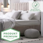 Prześcieradło bambusowe satyna bawełniana 220x260, w odcieniu chabrowym, położone na białym materacu. Złożone w estetycznym łóżku z szarym zagłówkiem, obok poduszki i plecionym, szarym pufem.