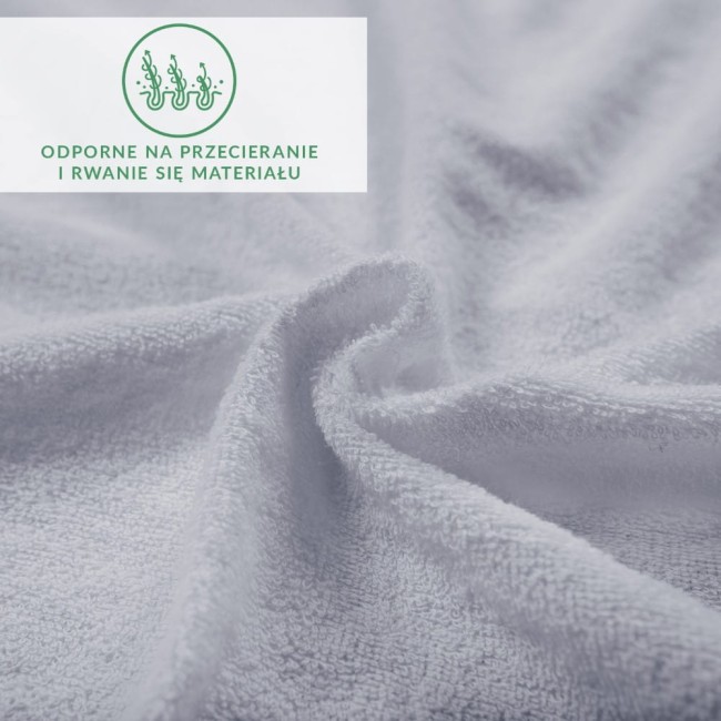 Prześcieradło frotte z gumką w kolorze popielatym, o gładkiej, teksturowanej powierzchni, rozłożone na płaskiej powierzchni. Widoczna struktura materiału. W prawym górnym rogu umieszczona zielona etykieta z napisem o odporności na przetarcia.