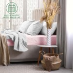 Prześcieradło frotte z gumką w kolorze róż kwarcowy, o wymiarach 200x220 cm. Widoczne na łóżku z szarymi poduszkami, otoczone dekoracjami, w tym wazonem i koszem. Produkt leży na materacu, dobrze dopasowany, z widoczną teksturą materiału.