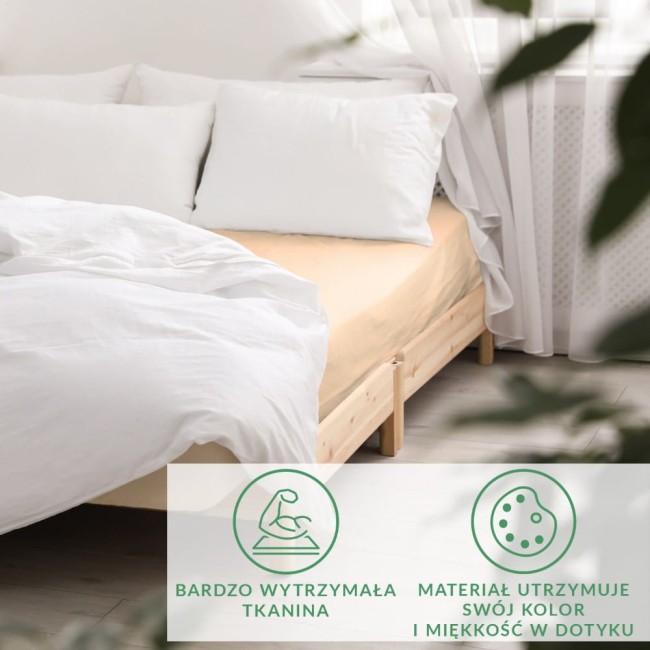 Prześcieradło satynowe z gumką w kolorze jasnego beżu, rozłożone na łóżku. Widoczne poduszki w białych poszewkach oraz drewniana rama. Tło jasne i naturalne, podkreślające materiał i kolor produktu.