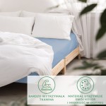 Prześcieradło satynowe z gumką 140x200 w kolorze błękitnym, rozłożone na łóżku, z widoczną naturalną drewnianą ramą. Otoczenie jasne, z białymi poduszkami i zasłonami, co podkreśla kolor prześcieradła. Materiał gładki i miękki.