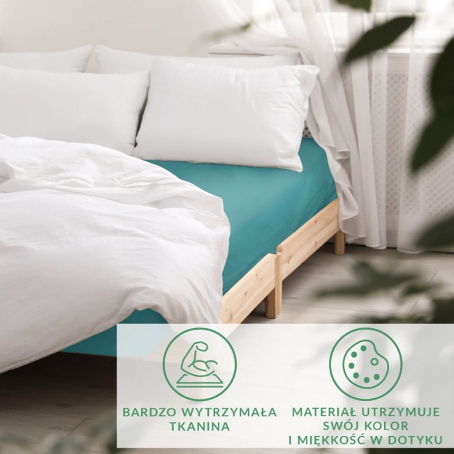 Prześcieradło satynowe z gumką o wymiarach 160x200 w kolorze ciemnego turkusu, rozłożone na łóżku z białą pościelą. Widoczne jasne poduszki w tle oraz delikatne zasłony. Tło jasne, minimalistyczne, podkreślające kolor prześcieradła.