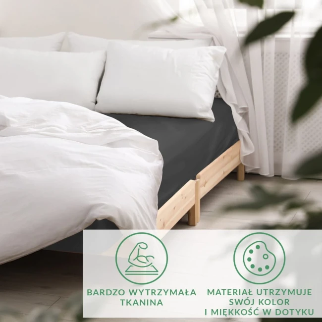 Prześcieradło satynowe z gumką 160x200 w kolorze czarnym, leżące na łóżku z naturalnym drewnianym stelażem. W tle widoczne białe poduszki i zasłony. Produkt akcentuje gładką fakturę materiału, lekko połyskującego w świetle.