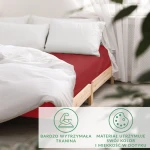 Prześcieradło satynowe z gumką w kolorze czerwonym, rozmiar 180x200, rozłożone na łóżku z białą pościelą i poduszkami. Ujęcie z boku, z widoczną fakturą tkaniny oraz charakterystycznym dopasowaniem do materaca. Tło minimalistyczne, drewniana rama łóżka.