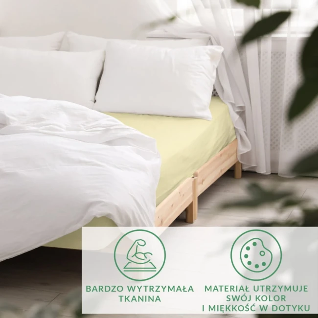 Prześcieradło satynowe z gumką 180x200 w kolorze kremowym, rozłożone na łóżku z białą pościelą. Wykonane z trwałej tkaniny, posiada gładką, miękką fakturę. Widoczne w tle naturalne światło i białe zasłony.