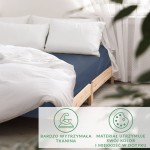 Prześcieradło satynowe z gumką w kolorze chabrowym, rozłożone na łóżku z naturalnym drewnem, z widocznymi białymi poduszkami. Kąt ujęcia z boku, tło jasne, przytulne wnętrze. Prześcieradło jest gładkie, delikatnie błyszczące, idealne do sypialni.