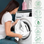 Prześcieradło satynowe z gumką 200x220 w kolorze jasnego beżu, rozłożone i trzymane przez kobietę, wkładane do pralki. W tle widoczne butelki z detergentami. Instrukcje prania, suszenia, prasowania i konserwacji umieszczone obok ładowania pralki.