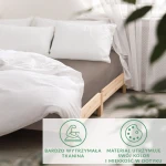 Prześcieradło satynowe z gumką w kolorze sepia, rozmiar 200x220, leży na łóżku z białą pościelą. W tle widoczne jaśniejsze poduszki oraz drewniana rama łóżka. Tkanina jest gładka i błyszcząca, wkomponowana w stonowaną aranżację wnętrza.