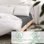 Prześcieradło satynowe z gumką w kolorze szarym, rozmiar 200x220 cm, naciągnięte na materac. Widoczna miękka faktura tkaniny, dopasowane do łóżka z białymi poduszkami i pościelą. Tło jasne, minimalistyczne, z naturalnym światłem.