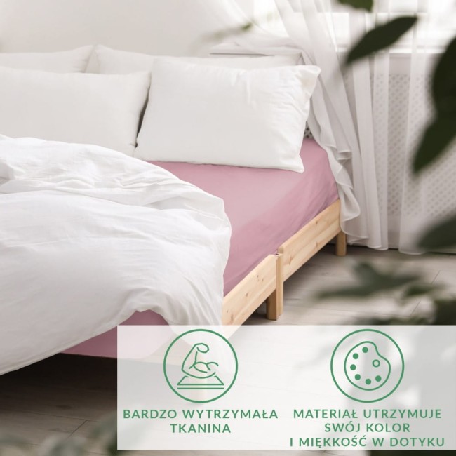 Prześcieradło satynowe w kolorze wrzosu, rozłożone na łóżku z naturalnym drewnem. Widać także białą poduszkę i kołdrę. Ujęcie z boku, otoczenie jasne, z delikatnymi firankami. Drobne napisy informacyjne o materiale i trwałości umieszczone na dole.