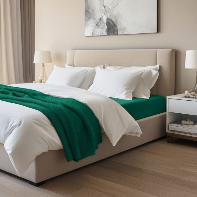 Prześcieradło jersey z elastanem w kolorze zielonym, rozmiar 160x200, leżące na łóżku z jasnym, eleganckim zagłówkiem. W tle widoczne białe poduszki i dekoracyjne akcesoria na szafce nocnej, na drewnianej podłodze.