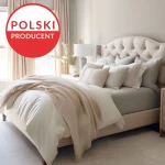 Prześcieradło jersey z elastanem 160x200 w kolorze niebieskim, rozłożone na łóżku. W tle widoczne jest jasne wnętrze z dużymi oknami, zasłonami i poduszkami w neutralnych odcieniach. Widoczne logo Polski Producent.