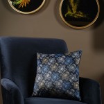 Poszewka dekoracyjna 43x43 w kolorze granatowym z kwiatowym wzorem. Zbliżenie na poszewkę leżącą na ciemnoniebieskim fotelu. Wzór przedstawia białe, niebieskie i złote kwiaty, wykonana z gładkiego materiału. Tło w odcieniach brązu.