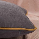 Poszewka dekoracyjna 40x40 w odcieniu szarości z lamówką w kolorze musztardowym, leżąca na delikatnie teksturowanym tle. Widoczny detal lamówki oraz tekstura materiału. Produkt w formacie kwadratu, przeznaczony do ozdobienia wnętrza.