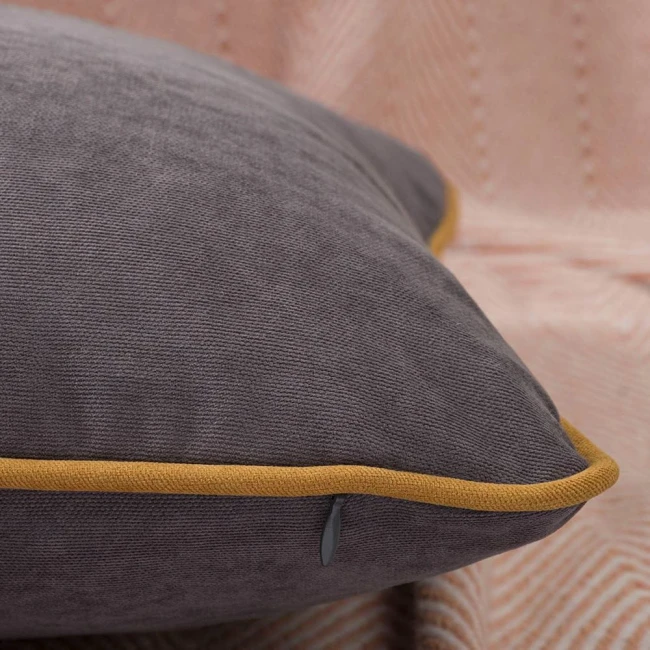Poszewka dekoracyjna 40x40 w odcieniu szarości z lamówką w kolorze musztardowym, leżąca na delikatnie teksturowanym tle. Widoczny detal lamówki oraz tekstura materiału. Produkt w formacie kwadratu, przeznaczony do ozdobienia wnętrza.