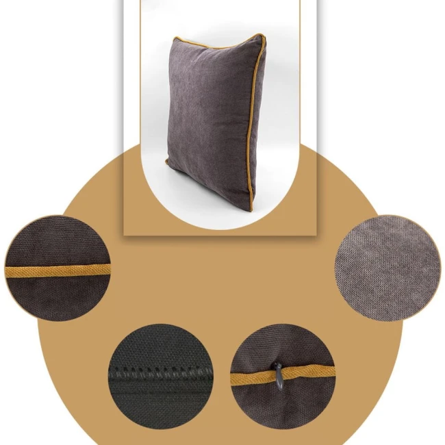 Poszewka dekoracyjna 40x40 cm w kolorze szarym z lamówką w kolorze musztardowym, widoczna z boku, lekko uniesiona. Tekstura materiału jest gładka, a lamówka wyraźnie zakończona. Widzoczne detale szycia oraz zamek. Tło jednolite, jasne.