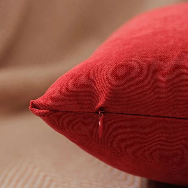 Poszewka dekoracyjna 45x45 w intensywnej czerwieni, gładka, z widocznym zamkiem. Produkt leży na tle w odcieniach brązu. Tekstura materiału widoczna z bliska, podkreślająca jego wytrzymałość. Zamek w tym samym kolorze co poszewka.