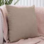 Poszewka dekoracyjna 45x45 cm, ciemno beżowa, gładka, leżąca na jasnym tle, otoczona miękkim, różowym kocem w wzór. Widoczna tekstura materiału, bez napisów i dekoracji. Idealna do aranżacji wnętrz.