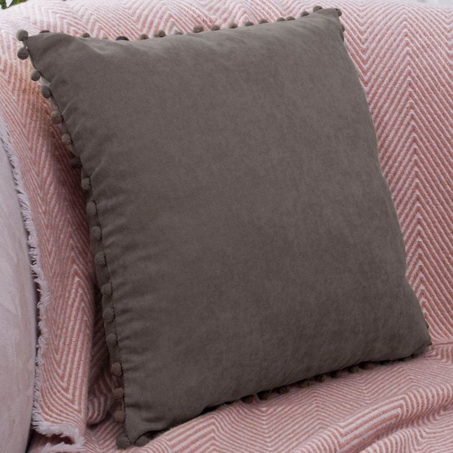 Poszewka dekoracyjna 45x45 szara, wykonana z miękkiego materiału, z dekoracyjnymi pomponami wzdłuż krawędzi. Ułożona leżąco na różowym tle, które posiada wzór w zygzaki. Zbliżenie na teksturę tkaniny, subtelnie podkreślającą kontrast z tłem.