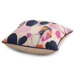 Poszewka dekoracyjna 43x43 cm w kolorze kremowym z artystycznymi, kolorowymi plamami w odcieniach różu, granatu i pomarańczy. Produkt leży na płaskiej powierzchni, pokazując szczegóły wzoru oraz kontrastującą krawędź.