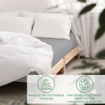 Prześcieradło satynowe bez gumki 200x220 w kolorze popielatym leży na łóżku z naturalnego drewna. Widoczne są białe poduszki oraz lekko rozłożona kołdra. Tło jest jasne z firankami w oknie, nadając przytulną atmosferę.