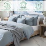 Prześcieradło satynowe bez gumki 200x220 w kolorze popielatym, leżące na łóżku z poduszkami w odcieniach błękitu. Widoczna miękka tkanina, na krawędzi lekko prześwitująca, z towarzyszącym szarym pledem. Tło neutralne, minimalistyczne wnętrze.