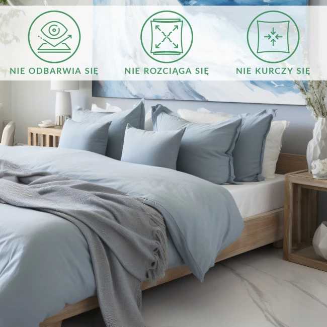 Prześcieradło satynowe bez gumki 200x220 w kolorze popielatym, leżące na łóżku z poduszkami w odcieniach błękitu. Widoczna miękka tkanina, na krawędzi lekko prześwitująca, z towarzyszącym szarym pledem. Tło neutralne, minimalistyczne wnętrze.