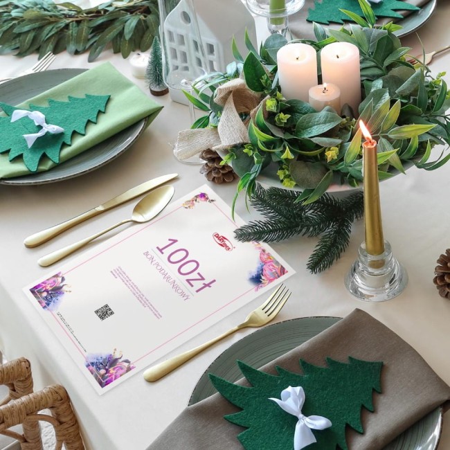 Karta podarunkowa o wartości 100 zł leży na stołowej, jasnej tkaninie. Na górze widać kolorowe ozdobne motywy.