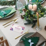 Karta podarunkowa o wartości 400 zł leży na beżowym obrusie, otoczona dekoracyjnymi elementami stołowymi, takimi jak sztućce złotego koloru, zielone serwetki w kształcie choinek oraz ozdobna świeczka. W tle widoczne rośliny dekoracyjne.